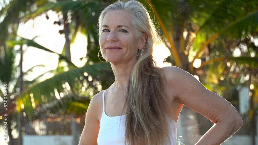 Smiling woman looks off camera and then nods in agreement and then looks off camera again with sun and palm tree behind her.
