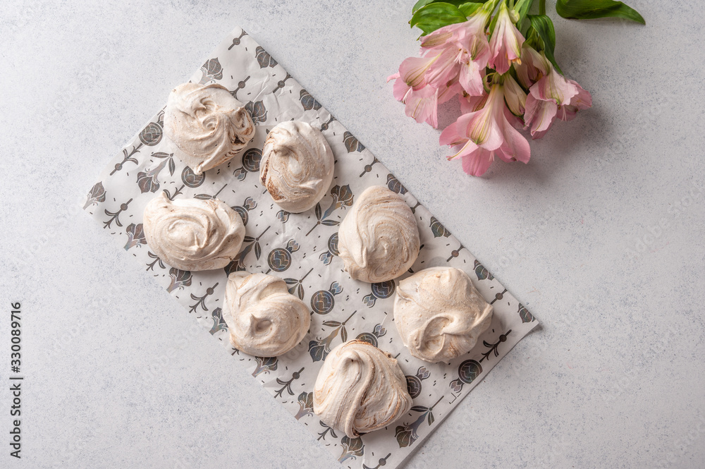 Homemade popular eggs dessert meringue on a pastry paper on light background. Next to pink flower. Copy space