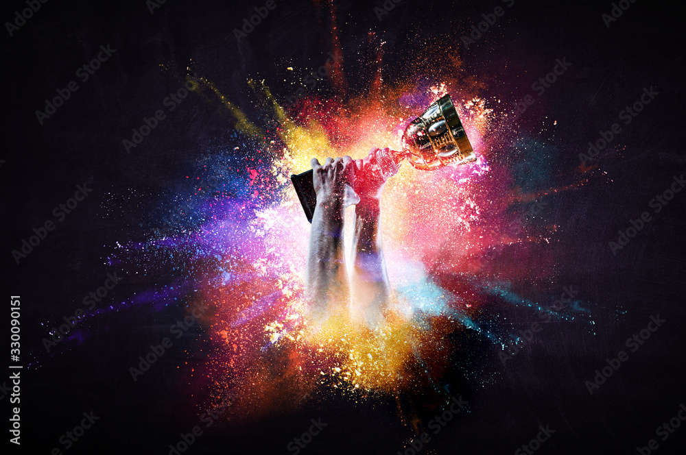 Hands holding champion cup on colourful splashes background. Mixed media - obrazy, fototapety, plakaty 