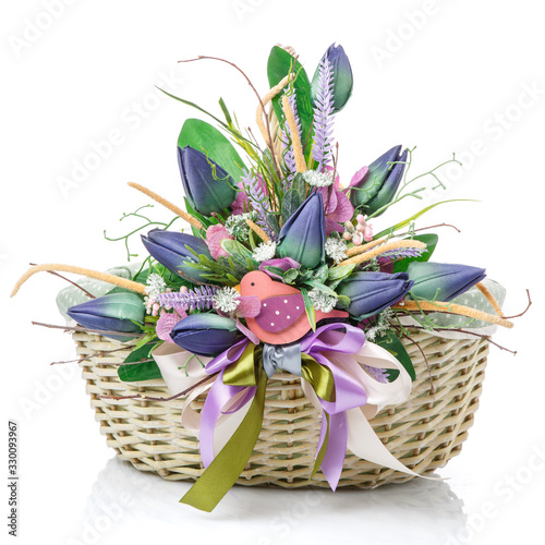 Easter basket on white background. Decorated with large decoration of blue tulips  greenery and decorative wooden bird.