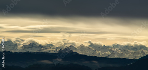 Dramatic landscape of snowy mountain tops in the Swiss alps as seen from the Zurich area late afternoon sun light illuminating from behind a thick sheet of clouds