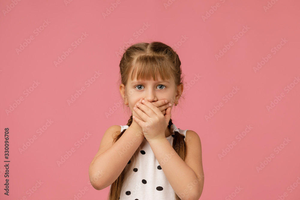 beautiful little girl in dress asking to be quiet. child closes her mouth with her hand. I will not tell anyone beautiful little girl in dress asking to be quiet. child closes her mouth with her hand. I will not tell anyone