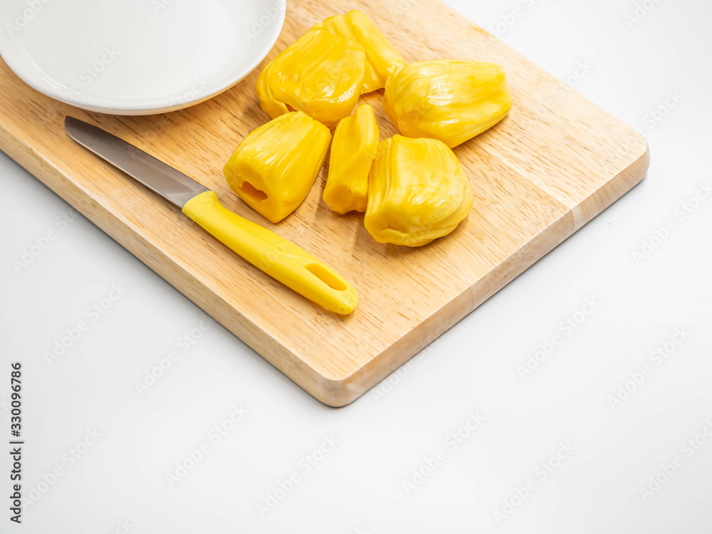 Closeup of yellow ripe jackfruit, knife, white ceramic dish on wooden cutting board in the kitchen or restaurant. Closeup of yellow ripe jackfruit, knife, white ceramic dish on wooden cutting board in the kitchen or restaurant.