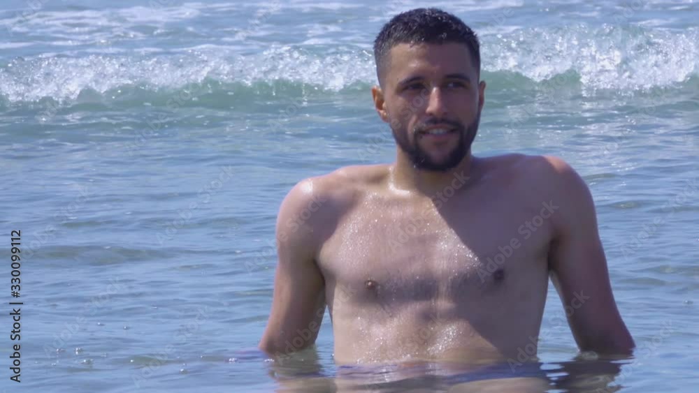 Young handsome man is sitting in the waves of the sea surf and enjoys a sea vacation Young handsome man is sitting in the waves of the sea surf and enjoys a sea vacation
