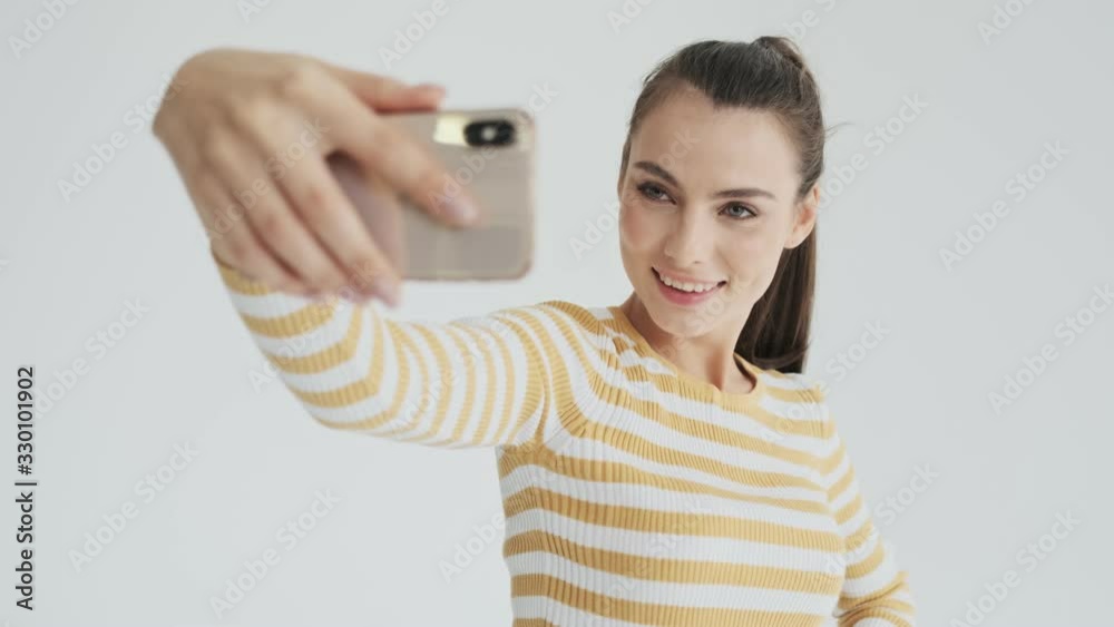 A charming young woman is sending an air kiss to the selfie camera isolated over white background in studio A charming young woman is sending an air kiss to the selfie camera isolated over white background in studio