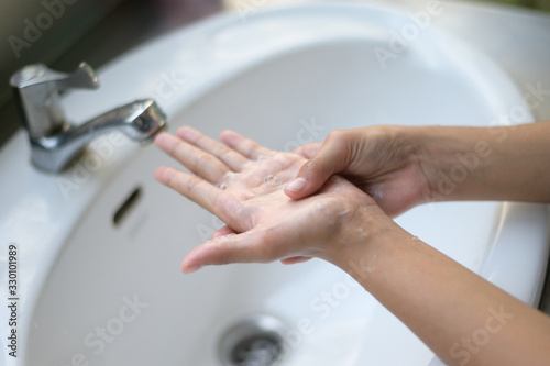 Asian Young woman washing hands with soap over sink in bathroom closeup hand.
