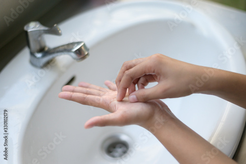 Asian Young woman washing hands with soap over sink in bathroom closeup hand.