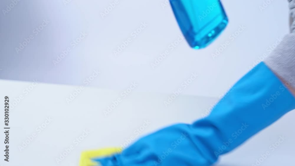 Young woman housekeeper is doing cleaning white table in apron with blue gloves, spray cleaner, wet yellow rag, close up, copy space, blank design concept. Young woman housekeeper is doing cleaning white table in apron with blue gloves, spray cleaner, wet yellow rag, close up, copy space, blank design concept.