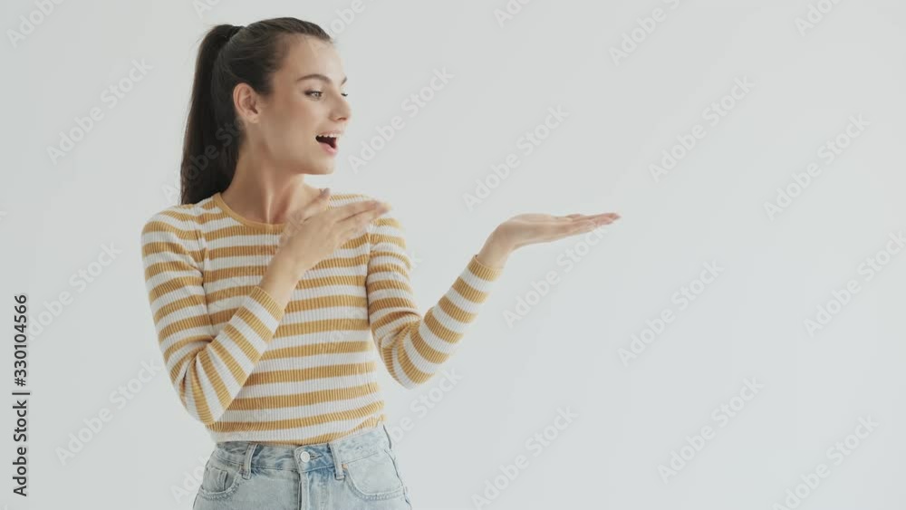 A beautiful smiling nice young woman is pointing to the free space in your palm over white background in studio A beautiful smiling nice young woman is pointing to the free space in your palm over white background in studio