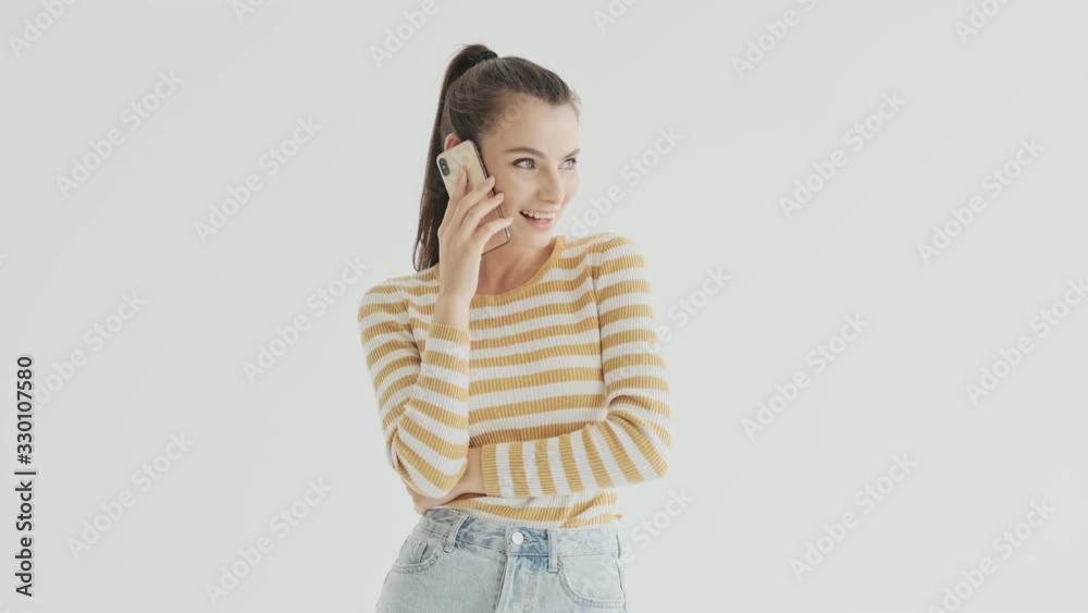 A beautiful smiling young woman is starting talking on the phone over white background in studio A beautiful smiling young woman is starting talking on the phone over white background in studio