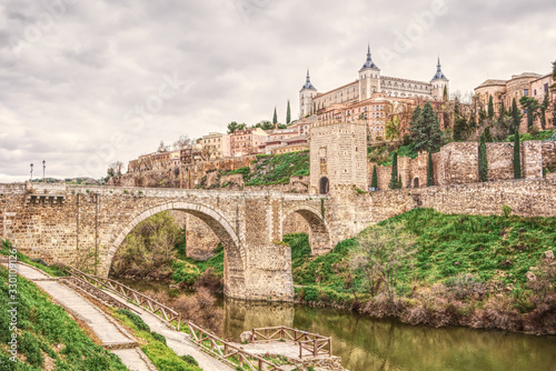 Cityscape of Toledo in Spain with Tagus River and Roman bridge Puente de Alcantara. Famous UNESCO World Heritage Site. The historic city in hdr art photography.
