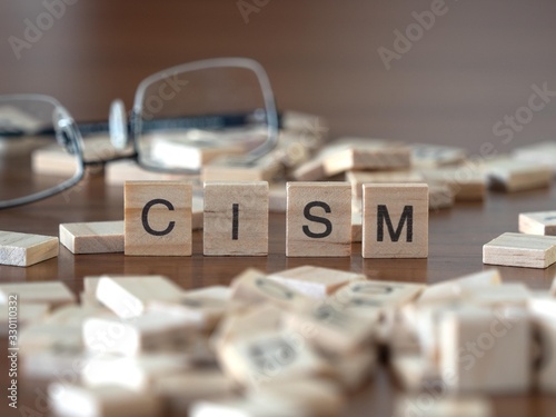 the acronym cism for Certified Information Security Manager concept represented by wooden letter tiles on a wooden table with glasses and a book