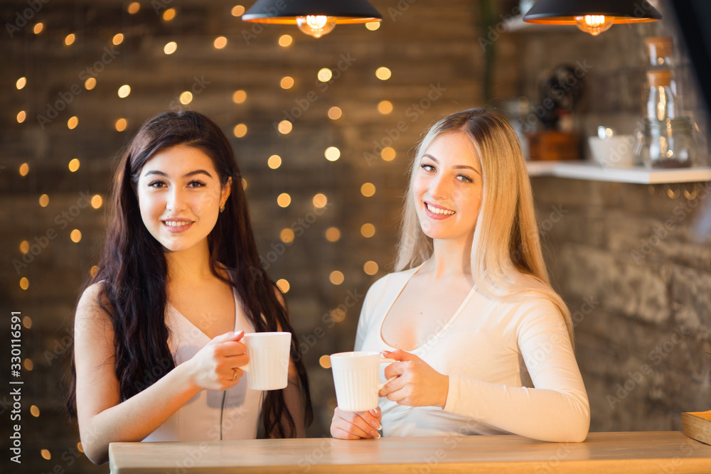 two beautiful young women are sitting at a table with mugs