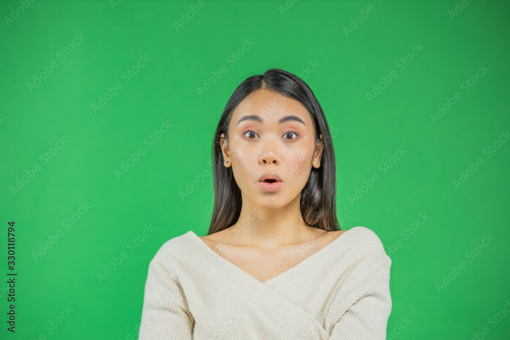 Obraz premium Surprise asian young woman pointing up isolated on green.