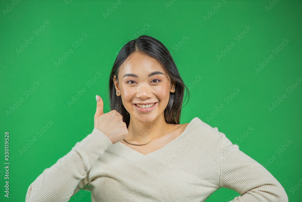 Anattractive young asian woman showing thumbs up over green background Anattractive young asian woman showing thumbs up over green background