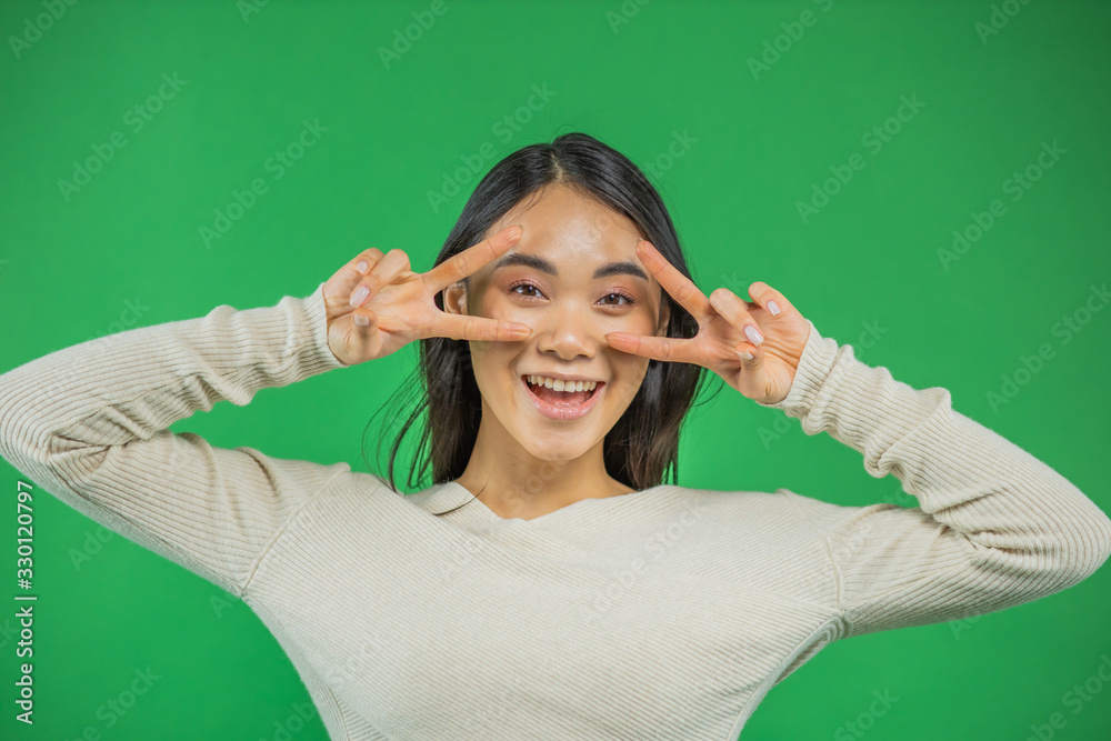 Portrait of an attractive young asian woman holds hands near his eyes green background Portrait of an attractive young asian woman holds hands near his eyes green background