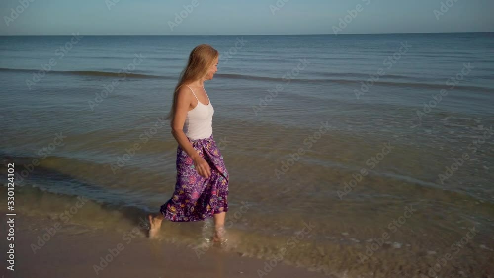 Slow motion of joyous mature woman walking along a beach shoreline at sunrise or sunset. Slow motion of joyous mature woman walking along a beach shoreline at sunrise or sunset.