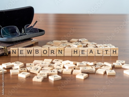 newborn health concept represented by wooden letter tiles on a wooden table with glasses and a book photo