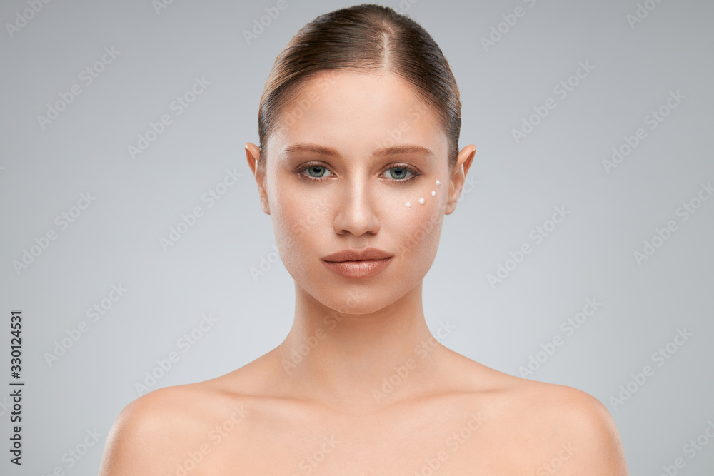Beautiful caucasian brunette posing in studio with creme on face while looking at camera.