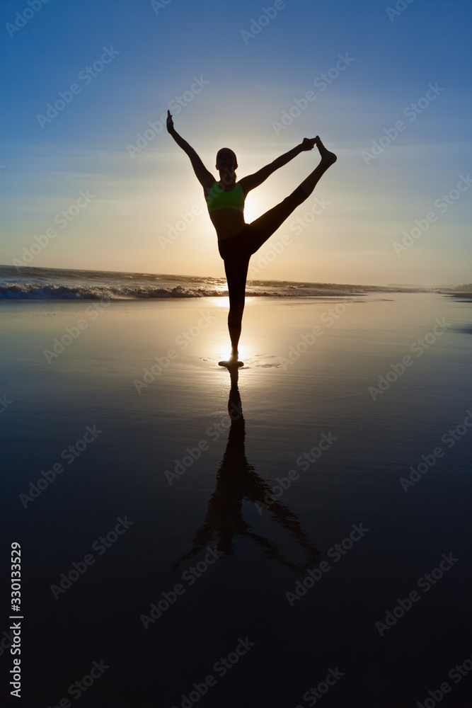 Silhouette of woman stretching at yoga pose on sunset beach