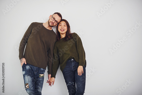 Happy multi ethnic couple in casual clothes is together indoors in the studio. Caucasian guy with asian girlfriend