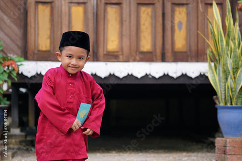 A Malay boy in Malay traditional cloth showing his happy reaction after receiving money pocket or 'Duit Raya' during Eid Fitri or Hari Raya celebration.