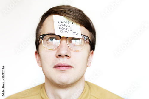April 1st Fools' day.Man in glasses with a sticker on his face.Sticker on forehead.Office jokes.Displeased face of man on white background. Office worker.Funny day.April fish.Trick at work. Raffle.