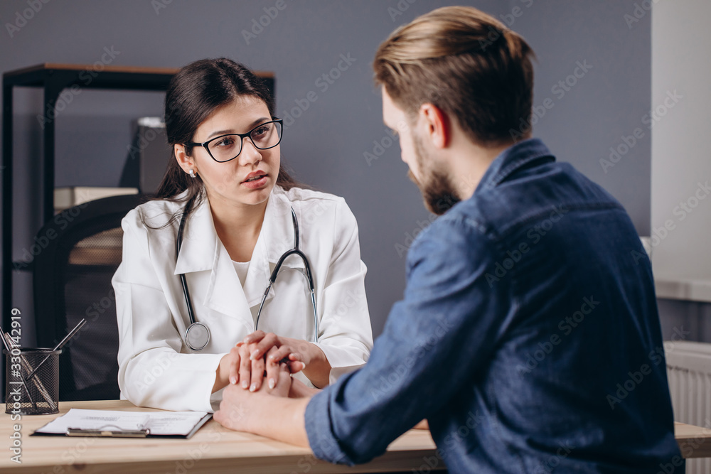 Sympathetic young female doctor cheering her patient up and holding his hands