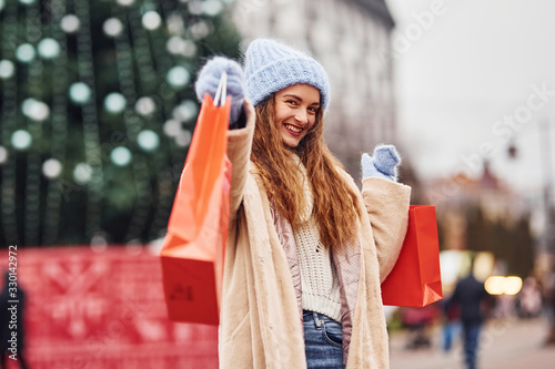Young girl in warm clothes with shopping bags in hands have a walk outdoors in the city