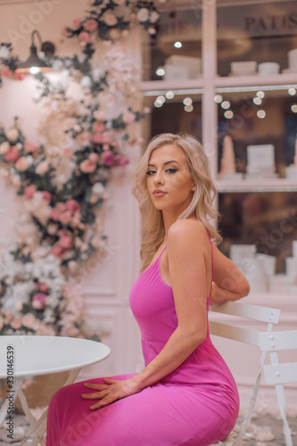 Attractive blonde in pink sexy dress posing among locations stylized as Paris cafe decorated with curly flowers