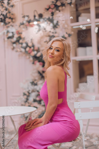 Attractive blonde in pink sexy dress posing among locations stylized as Paris cafe decorated with curly flowers