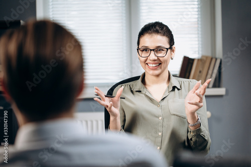 Portrait of smiling beautiful lady in stylish blouse and eyeglasses helping male patient to deal with emotional excitements. Concept of professional consultation and psychology