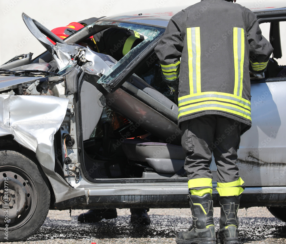 Fototapeta premium firefighter with uniofmr and helmet and a broken car