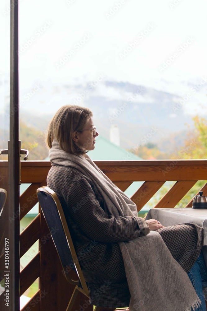 Girl in glasses and a checkered coat on a balcony of a chalet in the mountains in autumn. Girl in glasses and a checkered coat on a balcony of a chalet in the mountains in autumn.
