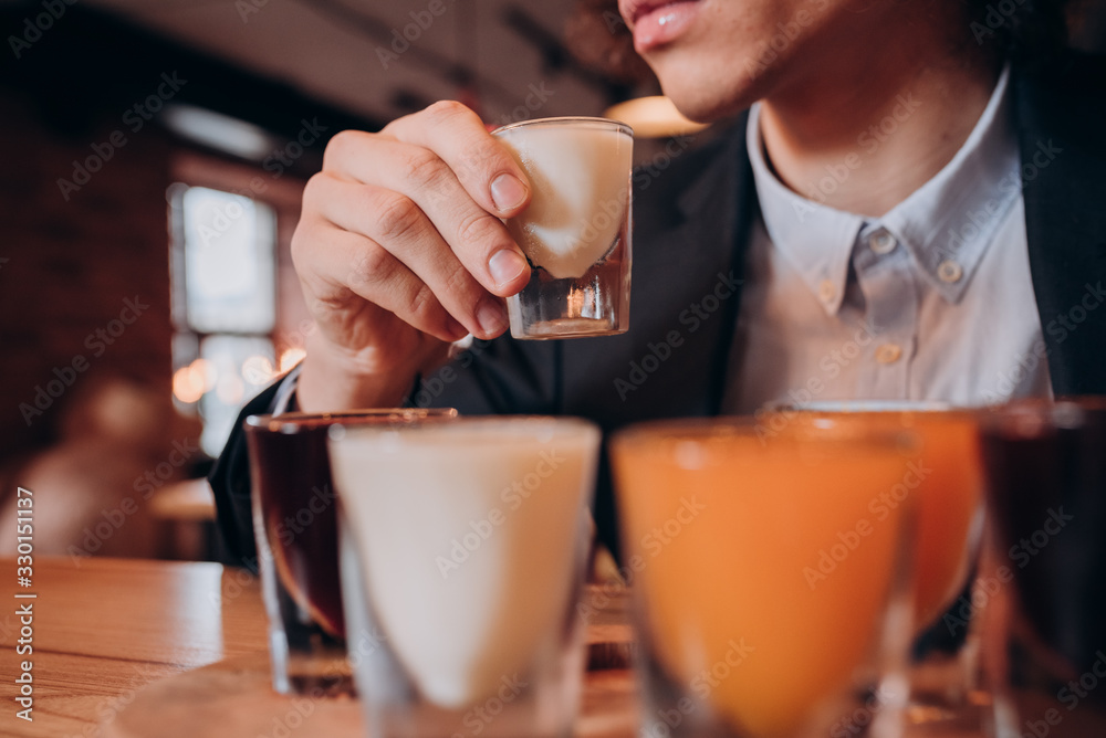 young curly-haired guy in a black suit drinking a liqueur in the bar young curly-haired guy in a black suit drinking a liqueur in the bar