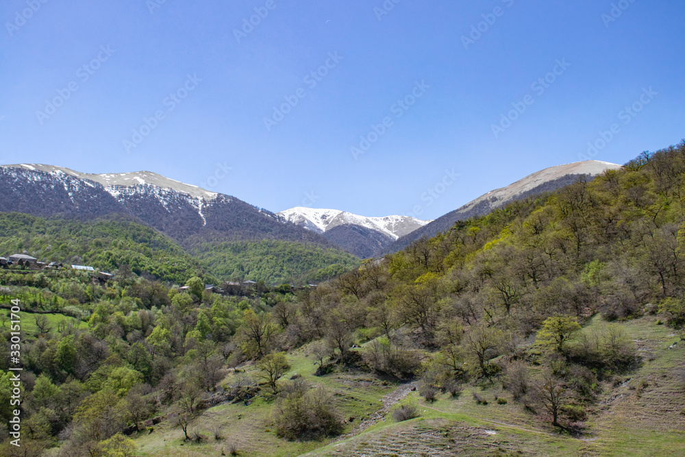 Armenia. Mountain landscape. The slopes of the mountains are covered with greenery, snowy peaks can be seen in the distance. White clouds on a blue sky.