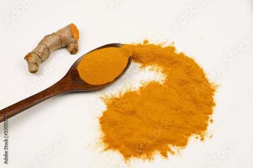 Turmeric powder in a wooden spoon and fresh turmeric root, isolated on a white background, is an ingredient in turmeric foods and ingredients in skin care products. Turmeric helps the skin to be stron photo