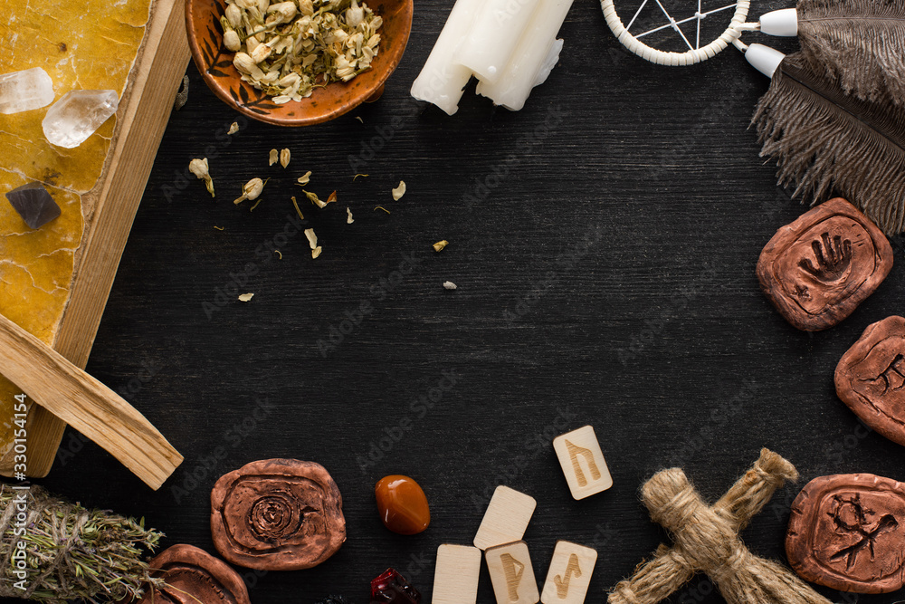 Top view of frame of shamanic amulets, book and candles on black wooden background