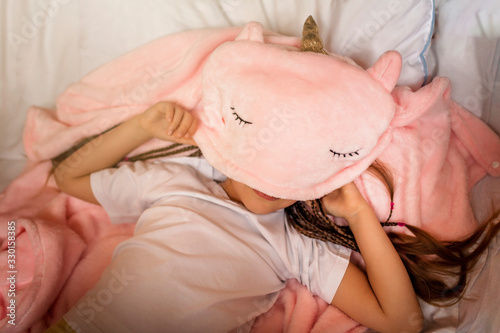 Top view of cute awaking girl with her toy animals wearing in light pink pajama with unicorn hoody