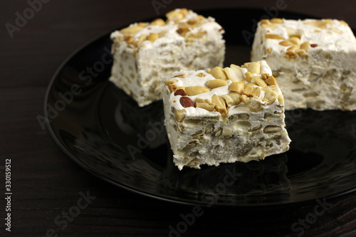 Pieces of sherbet or nougat with nuts in a plate on a dark wooden background