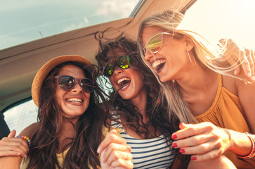 Three female friends enjoying traveling in the car. Sitting in rear seat and having fun on a road trip.