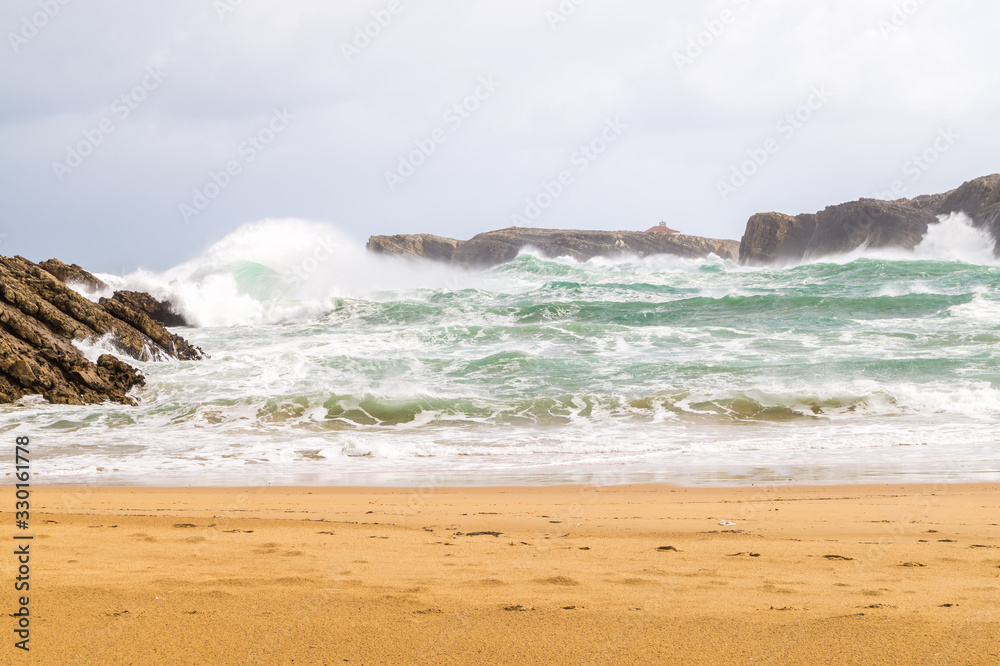 Beach in winter with dramatic cloudy sky, strong wind and waves