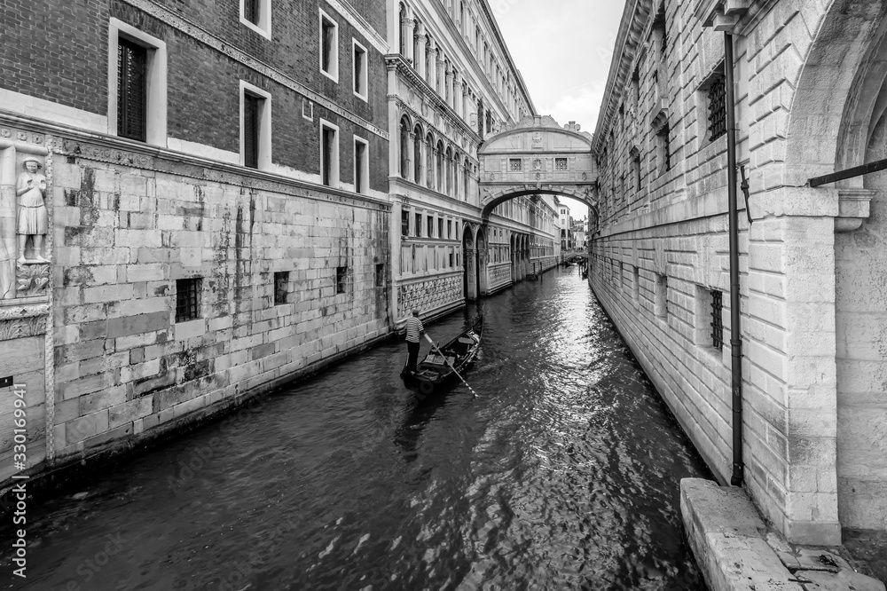 Fototapeta premium A typical Venetian gondola navigates the canal that passes under the famous Ponte dei Sospiri, Venice, Italy