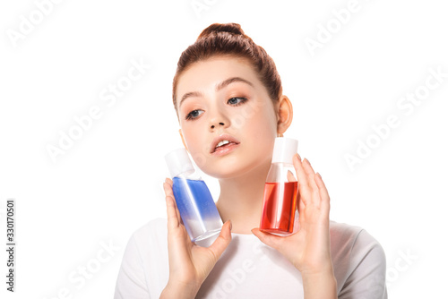 beautiful teenager holding two bottles with red and blue makeup removers, isolated on white