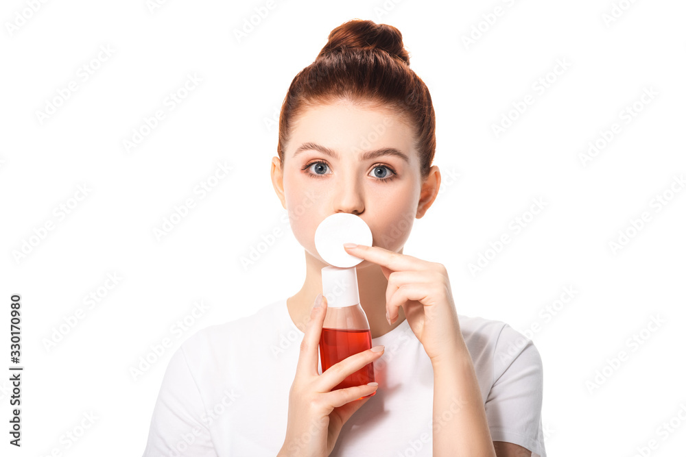surprised teenager with clean skin holding cotton sponge and bottle with red makeup remover, isolated on white surprised teenager with clean skin holding cotton sponge and bottle with red makeup remover, isolated on white
