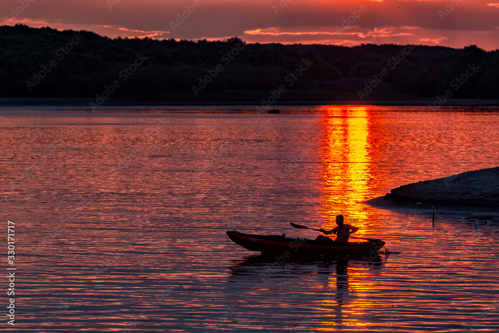 Silhouette of a sailor in a kayak canoe on the lake in the sunset light near an island, Danube River, Dobrogea, Romania