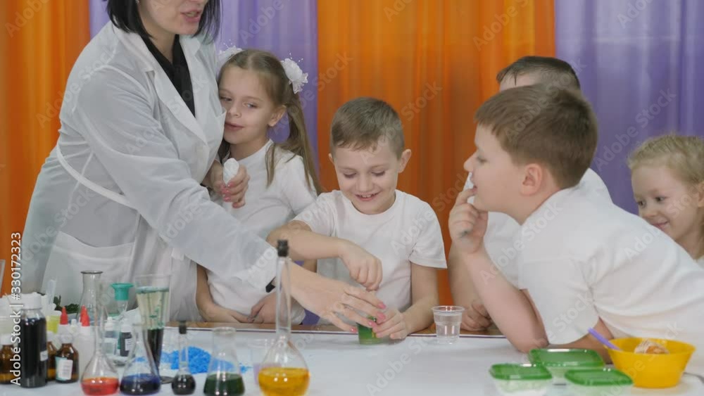 Chemical experiments for children. Woman pours a green substance into a white plastic bottle. Children are surprised. Room is filled with artificial smoke. Chemical experiments for children. Woman pours a green substance into a white plastic bottle. Children are surprised. Room is filled with artificial smoke.