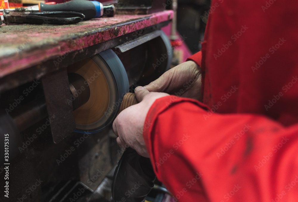 Shoemaker filing the rubber sole of a shoe with an electric disk