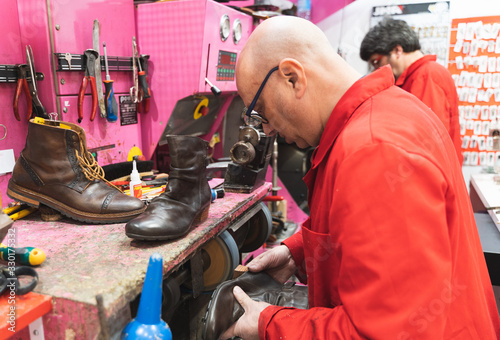 Shoemaker with a red uniform repairing the heel of a boot with an electric disk