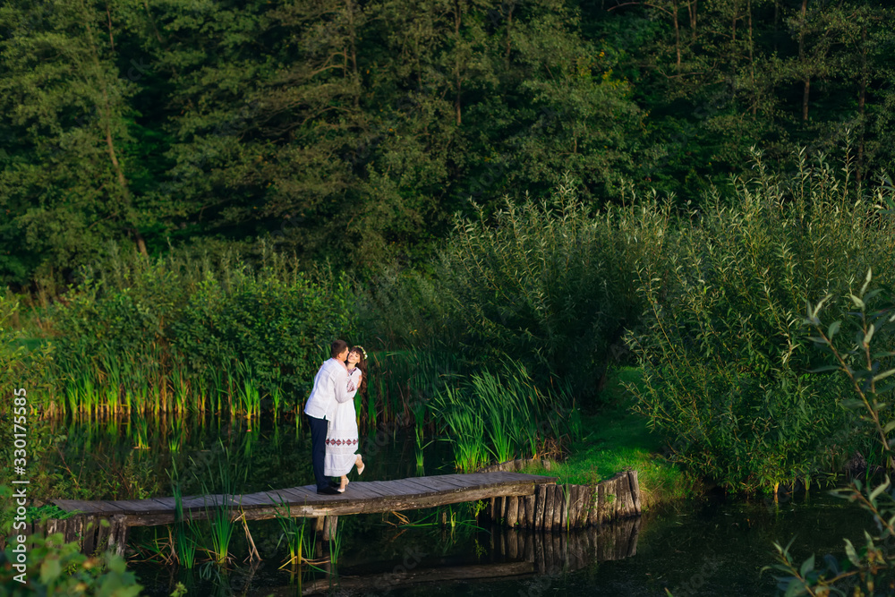 couple in embroidered clothes hugging on a wooden pier of a lake couple in embroidered clothes hugging on a wooden pier of a lake
